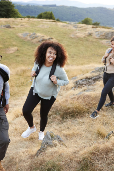 A multi ethnic group of five young adult friends smile while climbing to the summit during a mountain hike, close up